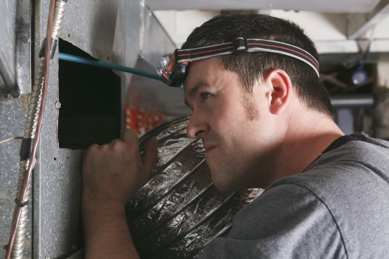 HVAC Technician performing maintenance on a furnace vent.
